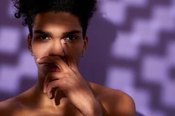 Portrait of young man face with hand on lips. Nude shirtless muscular model on purple background