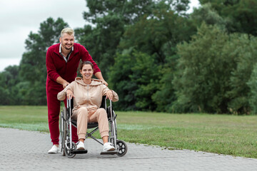 A girl on a wheelchair with a man spend time in the park. The young woman is disabled. The concept of a wheelchair, disabled person, full life, paralyzed, disabled person, health care.