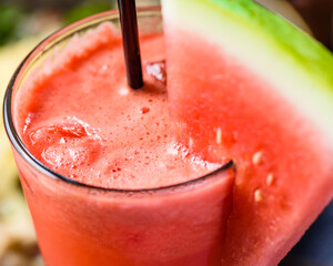 A top view of an orange and watermelon juice, with a black straw and slice of watermelon