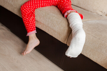 injured leg of an unrecognizable girl in a cast lying on the sofa at home