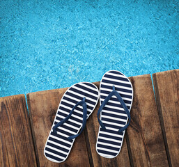Pair of flip flops on wooden deck near swimming pool, top view