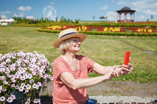 Happy senior woman taking selfie on smartphone at natural garden park during summer vacation, active retirement, fulfillment in every age, solo traveler, summer lifestyle