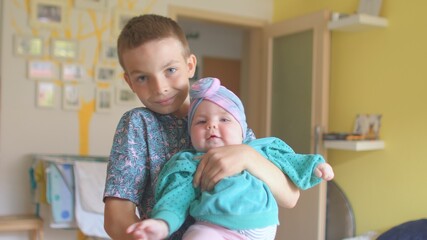 Obraz premium Close relationships are close relatives. Focus of attention to the camera. A teenager holds a little girl sister in the room. He kisses her. 