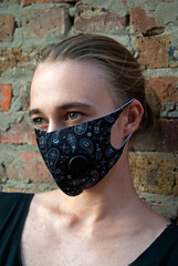 Security and Pandemic - Young woman wearing a reusable face shield against a brick wall.