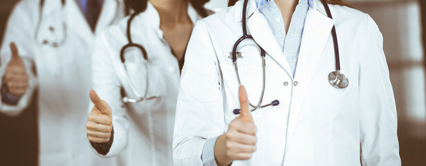 Group of doctors standing as a team with thumbs up in sunny clinic. Good news and Hope for a cure. Medicine concept during Coronavirus pandemic. Covid-2019