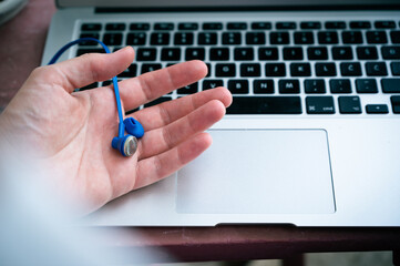 Hand holding blue earphone with detached ear tip, laptop keypad in background