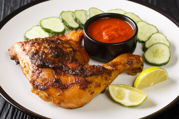 Ayam bakar is an Indonesian and Malaysian dish, consisting of charcoal grilled chicken served with cucumber and hot sauce closeup in the plate on the table. Horizontal