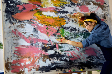 Inspired woman, female painter working on a large modern abstract oil painting, applying paint on canvas with fingers at home studio workshop