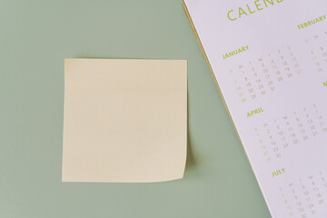blank yellow sticky note with yearly calendar on green background , top view