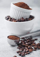 Fresh raw organic coffee beans in white bowl and powder on ligh background with round steel scoop.