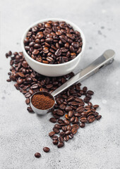 Coffee beans in white ceramic bowl with steel coffee soop on light background.