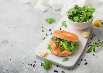 Organic healthy sandwich with salmon and bagel, cream cheese and wild rocket on light table