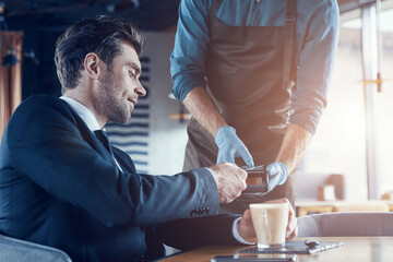 Handsome young businessman making a contactless payment while sitting in the restaurant