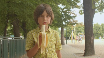Long hair teenager in shirt drawing a banana eats a banana. He chews food, increasing the strength...