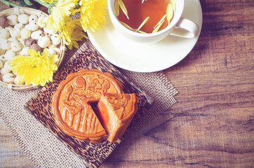 Top view of delicious homemade moon cake on wooden plate with tea cup and chrysanthemum flower in soft light vintage tone. For concept of Chinese Mid Autumn Festival celebration