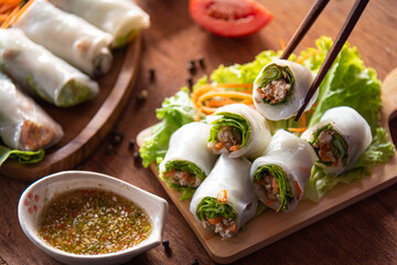 Tasty fresh spring rolls as tong  by chopsticks, stuffed minced pork serve with spicy sauce, Thai street food