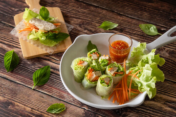 Asian fresh spring rolls with pork and shrimp, serve with spicy sauce, Thai street food on wooden background 