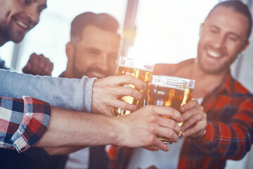 Happy young men in casual clothing toasting each other with beer and smiling