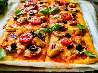 Pizza with white mushrooms, chicken nuggets, tomatoes, black olives and mozzarella on wooden background
