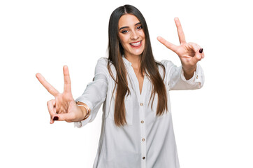 Young beautiful woman wearing casual white shirt smiling with tongue out showing fingers of both hands doing victory sign. number two.