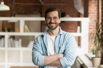 Successful 35s businessman male employee in eyeglasses casual clothes standing alone in modern office room look at camera pose with arms crossed. Portrait of company executive, business growth concept