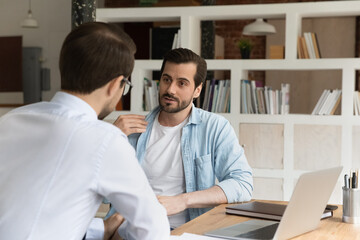 Obraz premium Businesspeople male staff members talking sit at workplace desk. Serious advisor consult client make offer at meeting in office, men colleagues share ideas, discuss new collaborative project concept