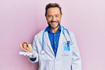 Middle age gynecologist man holding anatomical model of female uterus with fetus looking positive and happy standing and smiling with a confident smile showing teeth