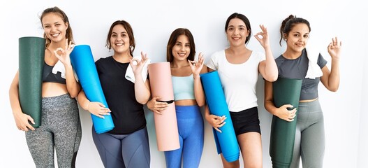 Obraz premium Group of women holding yoga mat standing over isolated background smiling positive doing ok sign with hand and fingers. successful expression.