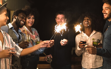 Happy young friends having fun with sparklers fireworks and drinking cocktails on house patio party - Youth people lifestyle and holidays concept