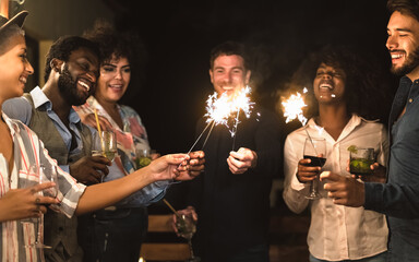 Happy young friends having fun with sparklers fireworks and drinking cocktails on house patio party...