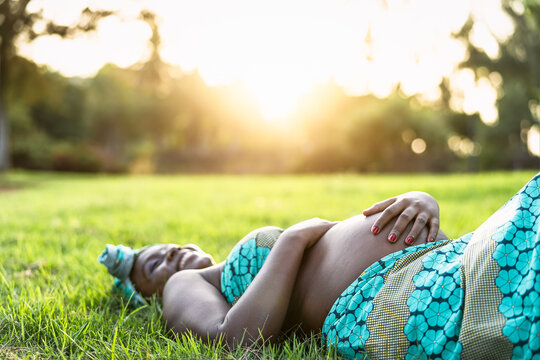 African pregnant woman lying on green grass park during sunset time - Maternity lifestyle concept