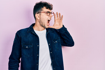 Young hispanic man wearing casual clothes and glasses shouting and screaming loud to side with hand on mouth. communication concept.