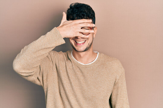 Young hispanic man wearing casual clothes and glasses smiling and laughing with hand on face covering eyes for surprise. blind concept.