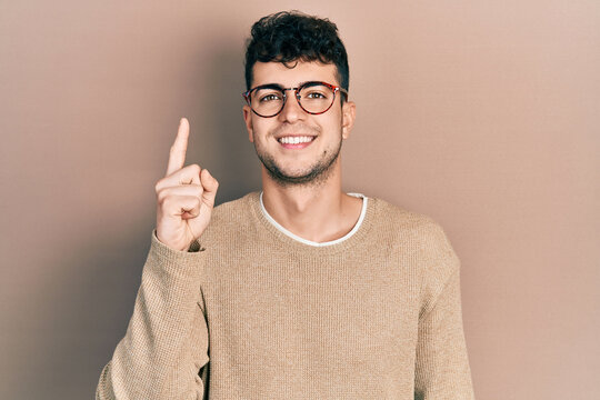 Young hispanic man wearing casual clothes and glasses pointing finger up with successful idea. exited and happy. number one.