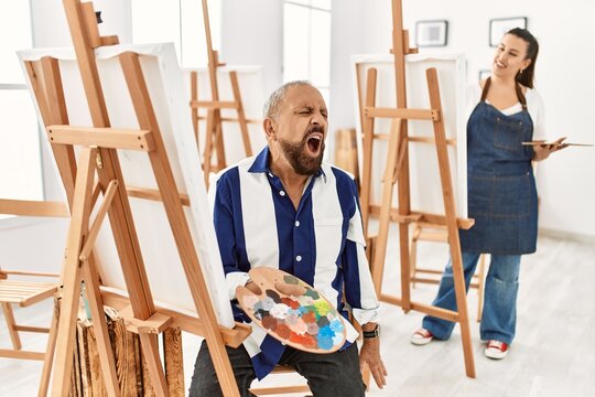 Senior artist man at art studio angry and mad screaming frustrated and furious, shouting with anger. rage and aggressive concept.