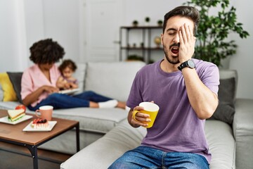 Hispanic father of interracial family drinking a cup coffee yawning tired covering half face, eye and mouth with hand. face hurts in pain.