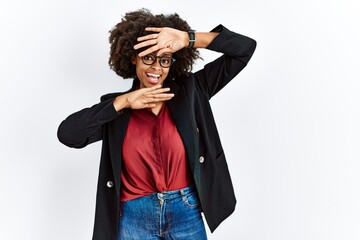 Fototapeta na wymiar African american woman with afro hair wearing business jacket and glasses smiling cheerful playing peek a boo with hands showing face. surprised and exited