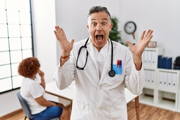 Middle age doctor man at the clinic with a patient celebrating crazy and amazed for success with arms raised and open eyes screaming excited. winner concept