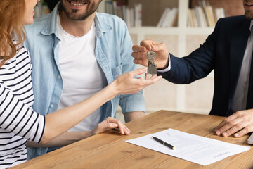 Cropped close up view happy couple receiving keys from new own property, finish meeting in real estate agency lead by realtor in formal suit. Bank mortgage for young family, selling, renting concept
