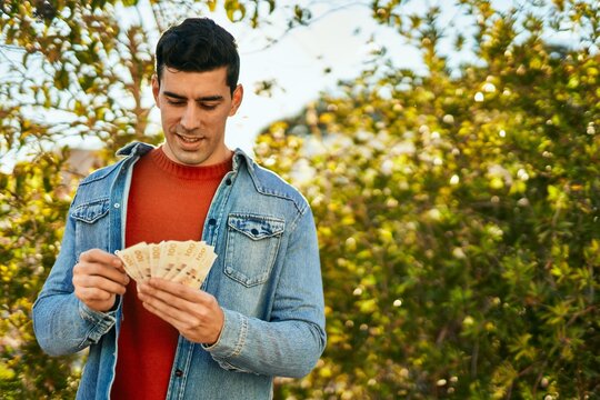 Young hispanic man smiling happy holding denmark krone banknotes at the city.
