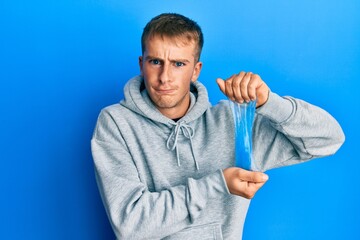 Young caucasian man holding slime skeptic and nervous, frowning upset because of problem. negative...