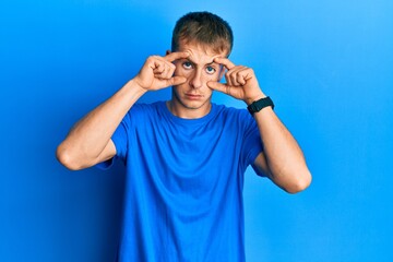 Young caucasian man wearing casual blue t shirt trying to open eyes with fingers, sleepy and tired for morning fatigue