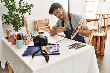 Fototapeta premium Young hispanic artist man smiling happy making online paint class at art studio.