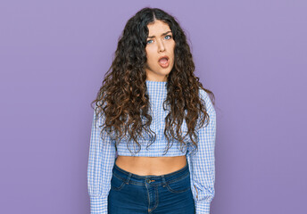 Young hispanic girl wearing casual clothes in shock face, looking skeptical and sarcastic,...