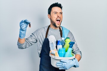 Young hispanic man holding cleaning products and cockroach angry and mad screaming frustrated and...