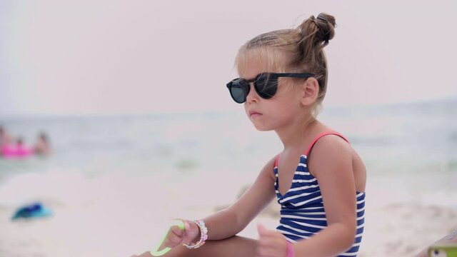 Little girl dressed stripped swimwear hold kite rope playing sea beach Summertime leisure Caucasian female child play alone 