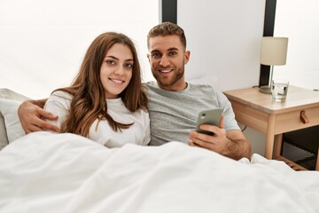 Fototapeta premium Young caucasian couple using smartphone lying on bed at home.