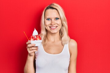 Beautiful caucasian blonde woman eating strawberry ice cream looking positive and happy standing and smiling with a confident smile showing teeth