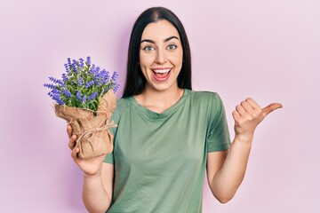 Beautiful woman with blue eyes holding lavender plant pointing thumb up to the side smiling happy with open mouth