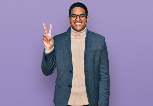 Young handsome hispanic man wearing business jacket and glasses smiling with happy face winking at the camera doing victory sign. number two.